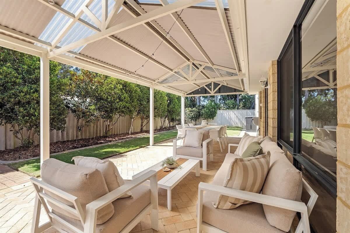 An outdoor patio with a covered seating area, including sofas and chairs, and a large window for natural light.