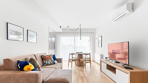 A modern living room with a sofa, a dining table, and a TV displaying "GUEST READY". - GuestReady - Seaside retreat - 4D (Matosinhos)