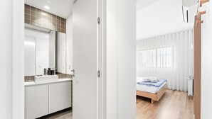 A modern bathroom with a large mirror, white cabinets, and a beige-tiled backsplash. - GuestReady - Seaside retreat - 4D (Matosinhos)