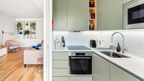 A modern kitchen with a built-in oven, a microwave, and a sink. There is a dining area with a pink sofa and a small table. - GuestReady - Seaside retreat - 4D (Matosinhos)