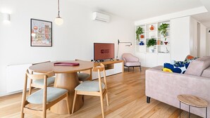 A modern living room with a wooden dining table, chairs, a sofa, and a TV. - GuestReady - Seaside retreat - 4D (Matosinhos)
