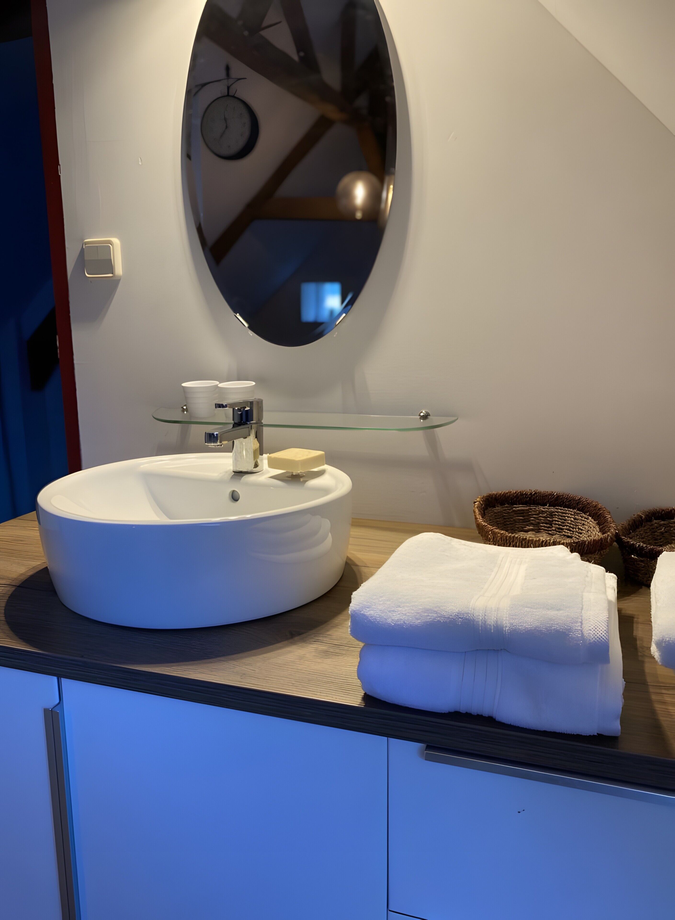 Ein Badezimmer mit einem runden weißen Waschbecken, einer Glasablage, einem Spiegel und einem Handtuch auf der Ablagefläche.