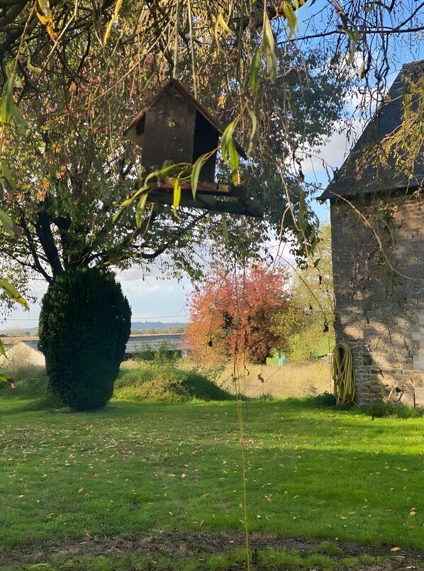 Un jardín con un comedero para pájaros, setos y un edificio de piedra.