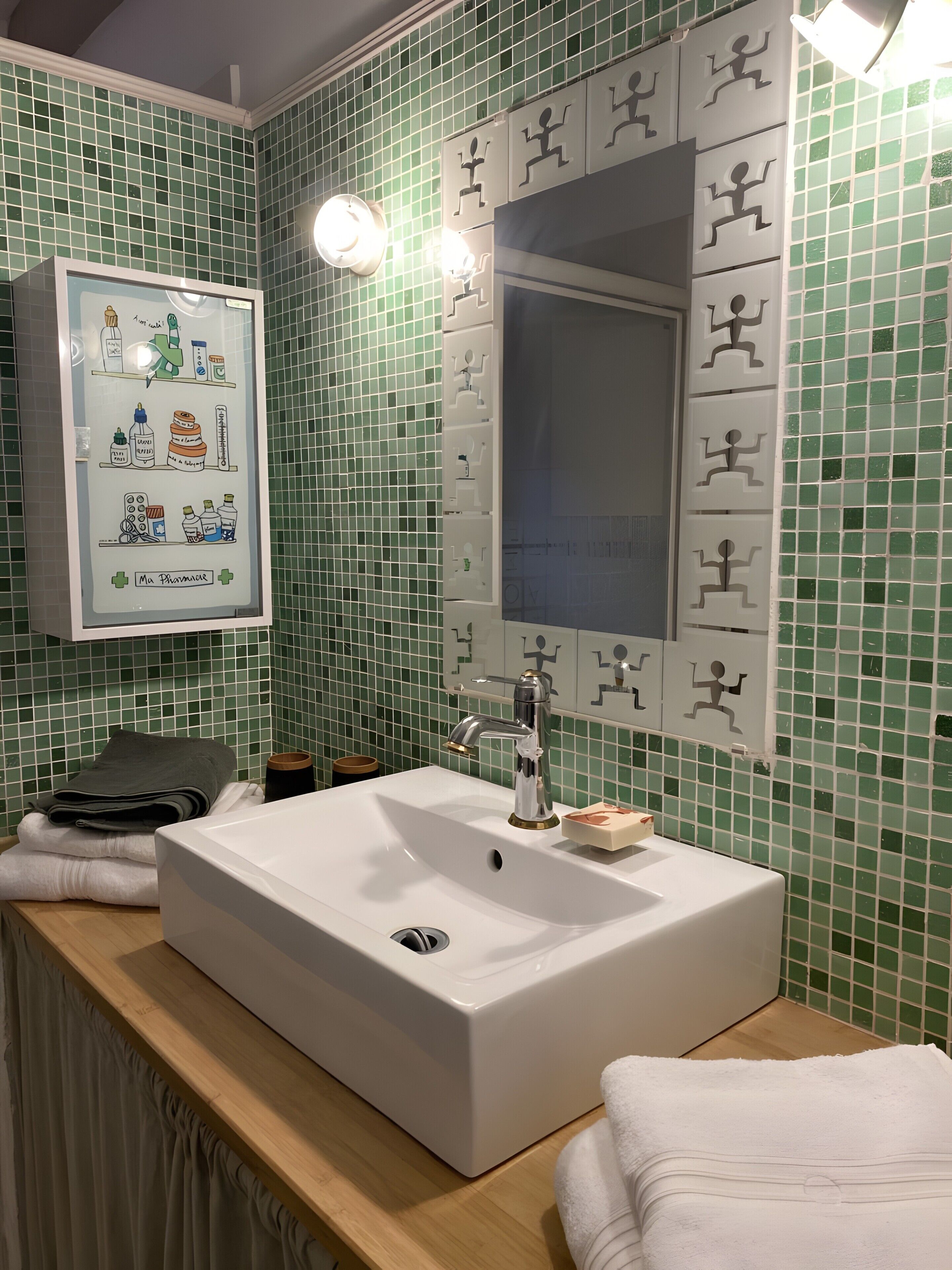 Ein Badezimmer mit einem weißen Waschbecken, grünen Fliesenwänden, einer gerahmten Illustration und einem Spiegel.