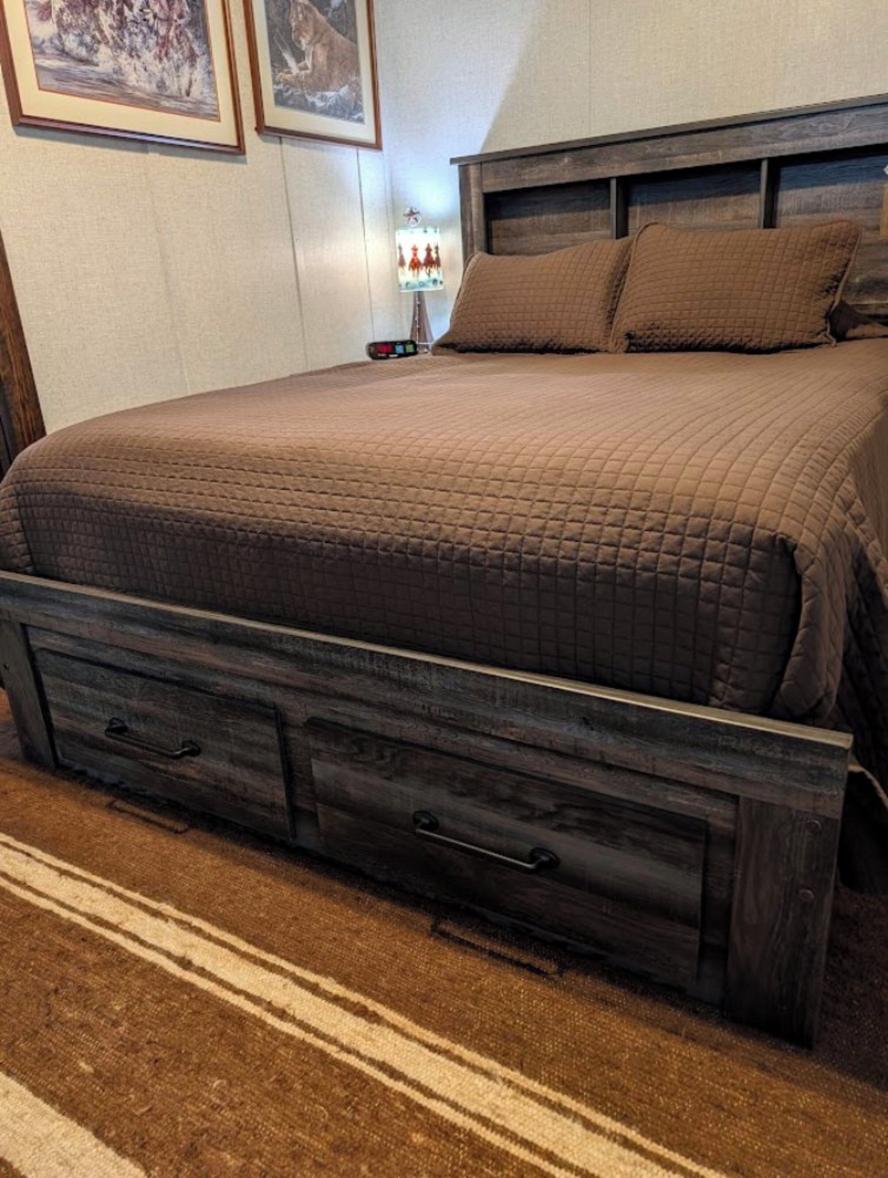 A bed with a quilted cover, a wooden headboard, and a nightstand with a lamp.