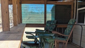 A wooden deck with a table and chairs, a window with a view, and a cat on the floor.