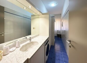 A modern bathroom with a large mirror, a sink, a washing machine, and a blue-tiled floor. - Matt's Home - One Bedroom Apartment, Sleeps 4 (Milano)