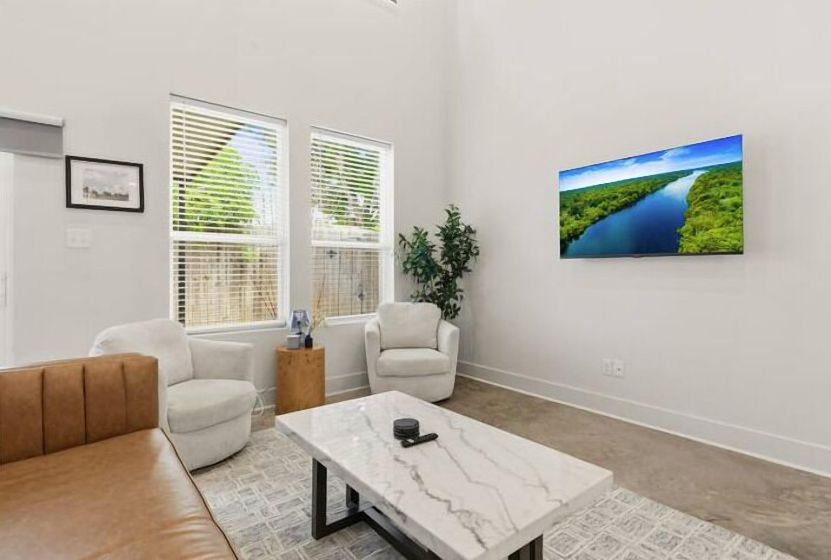 Ein modernes Wohnzimmer mit einem Marmortisch, weißen Sofas und einem großen Landschaftsbild an der Wand.