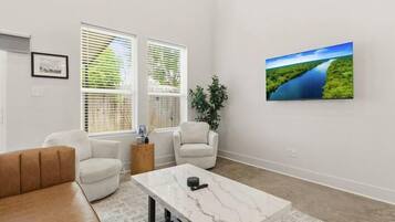 Ein modernes Wohnzimmer mit einem Marmortisch, weißen Sofas und einem großen Landschaftsbild an der Wand.