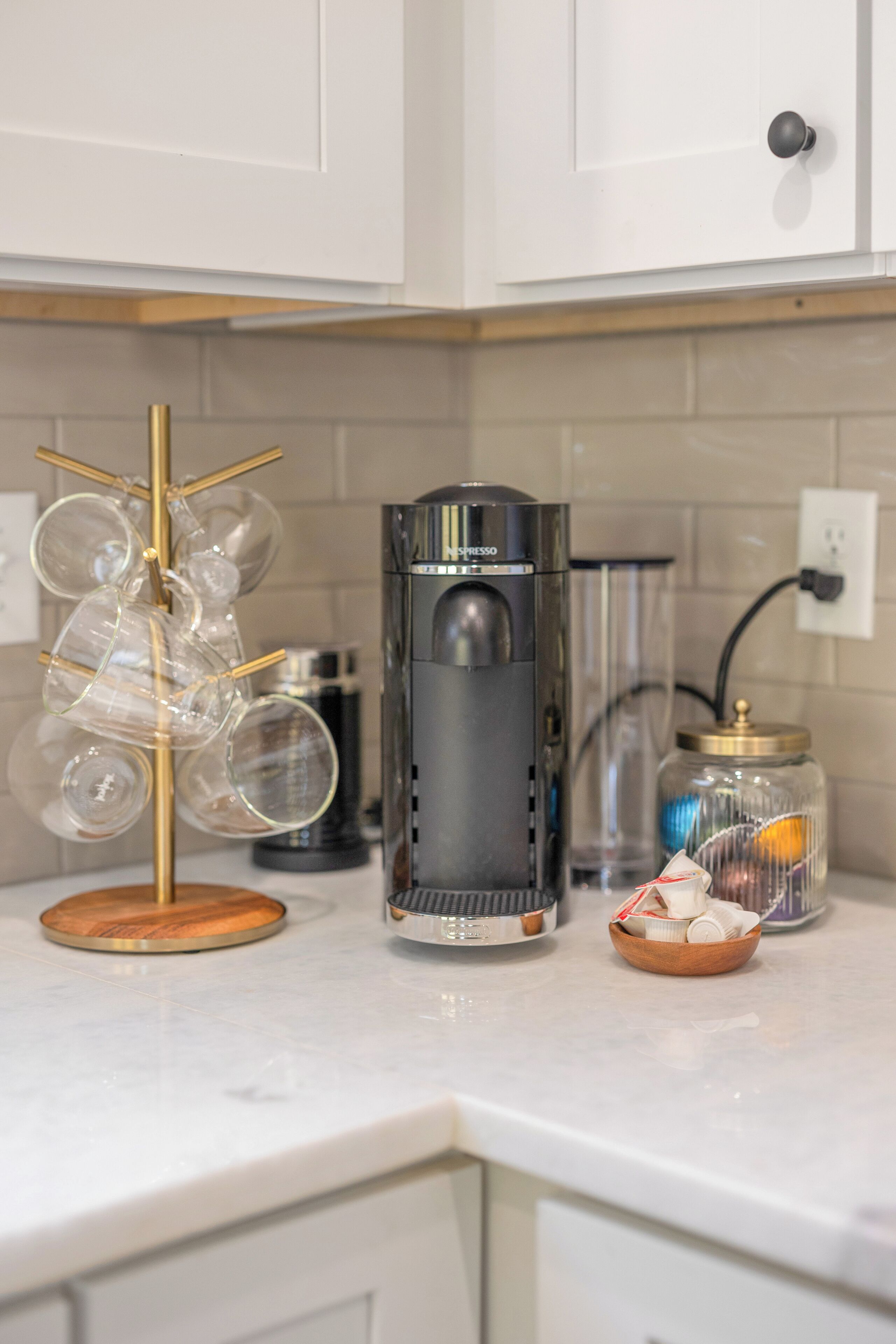 Una encimera de cocina con una cafetera, un tarro de cristal y un cuenco de utensilios.