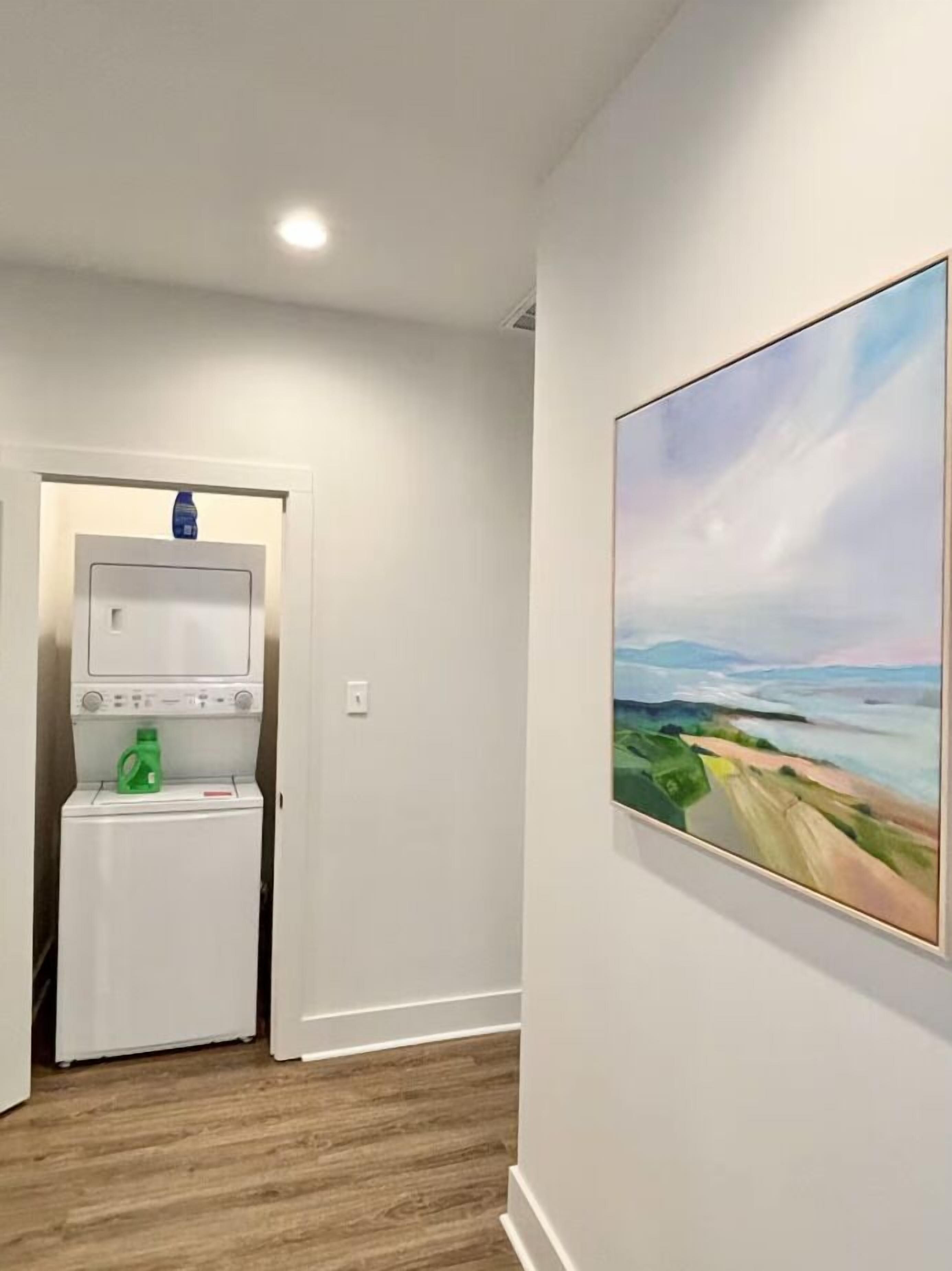 A laundry room with a washing machine and dryer, a door leading to another room, and a painting on the wall.