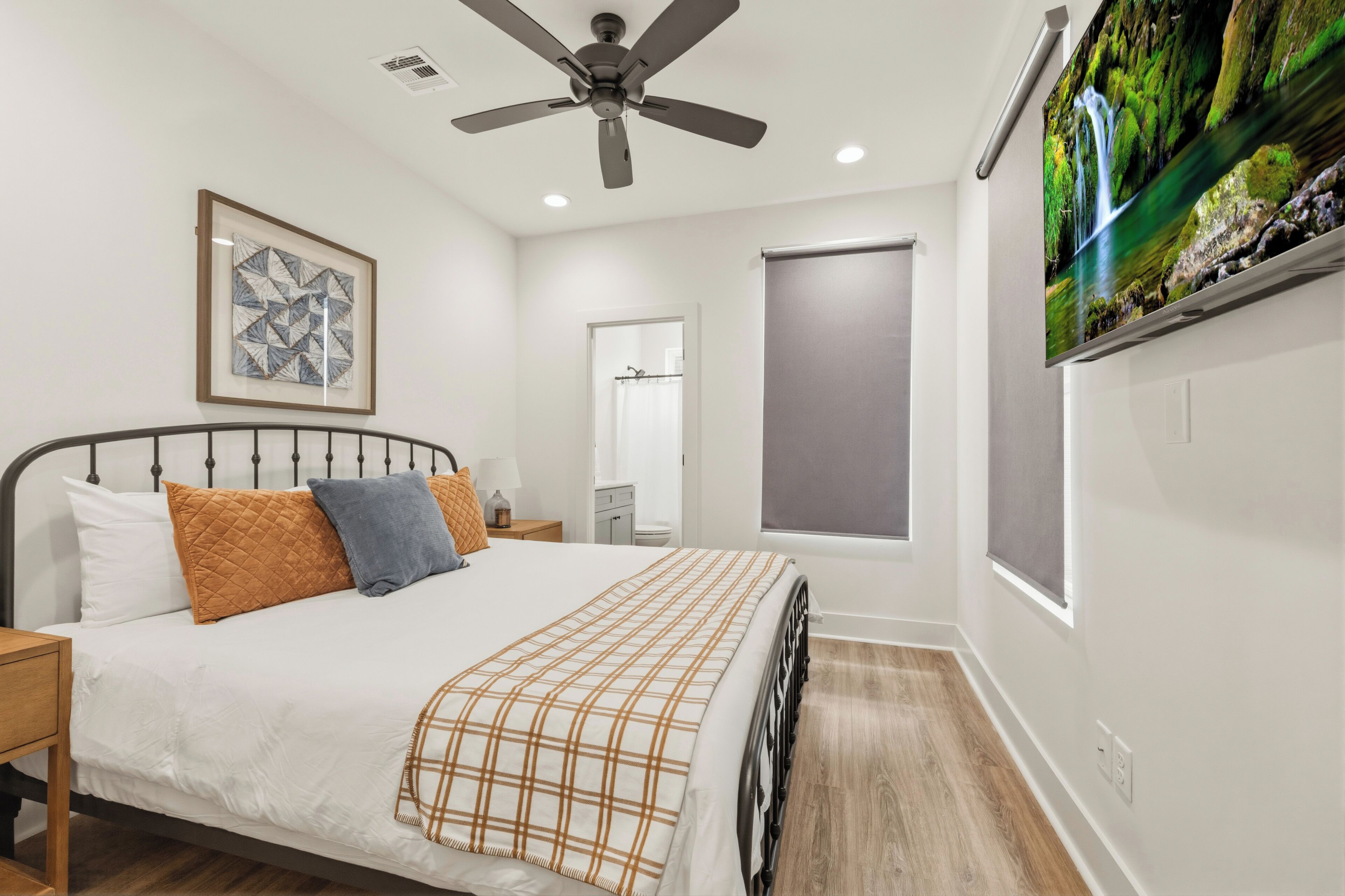 A bedroom with a bed, a ceiling fan, a TV, and a window.