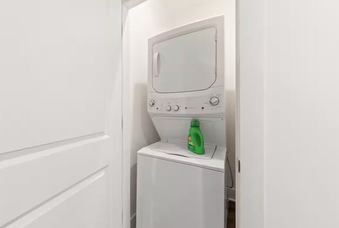 A compact, white laundry room with a washing machine and a detergent bottle.