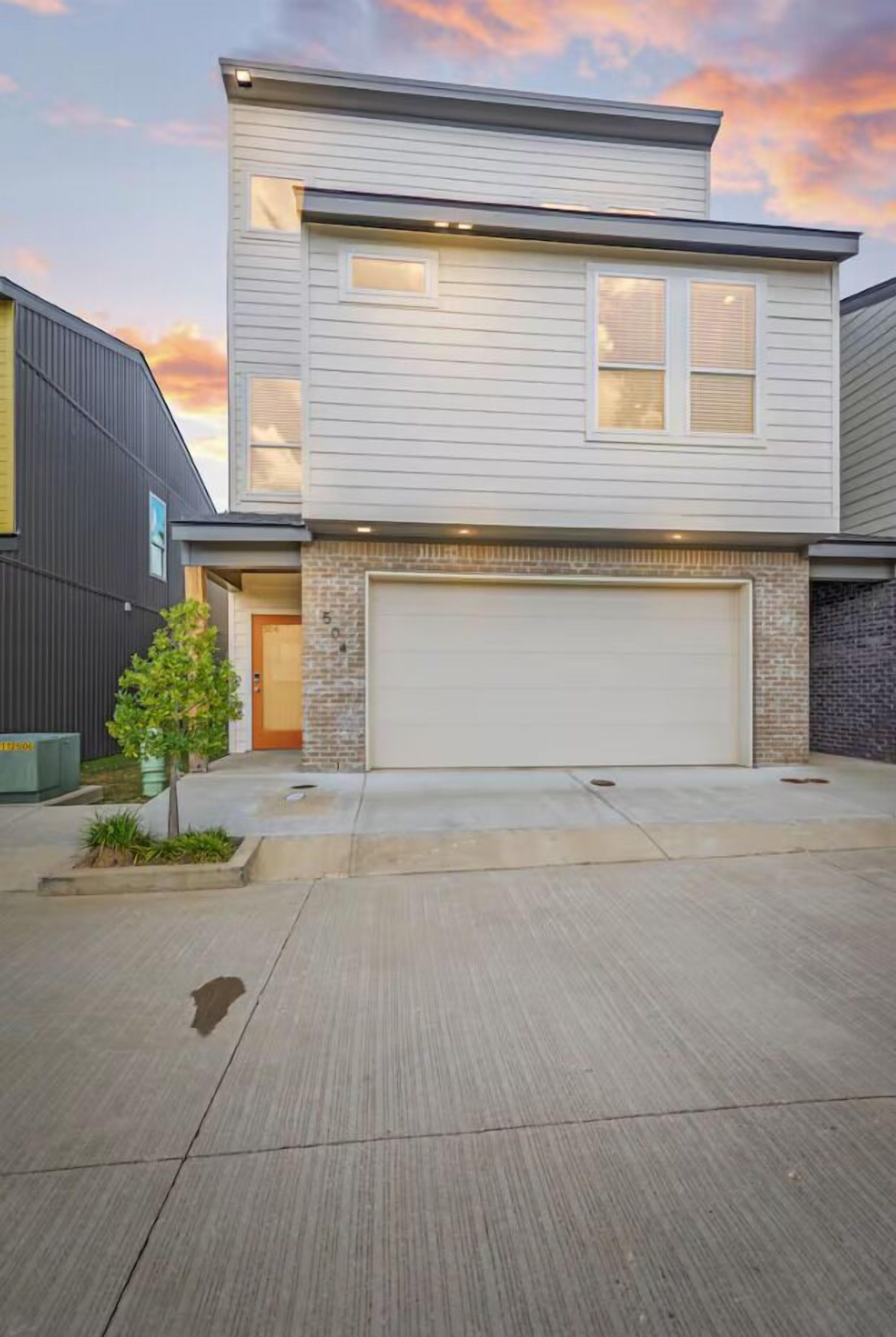 A two-story house with a garage, a small front yard, and a tree.