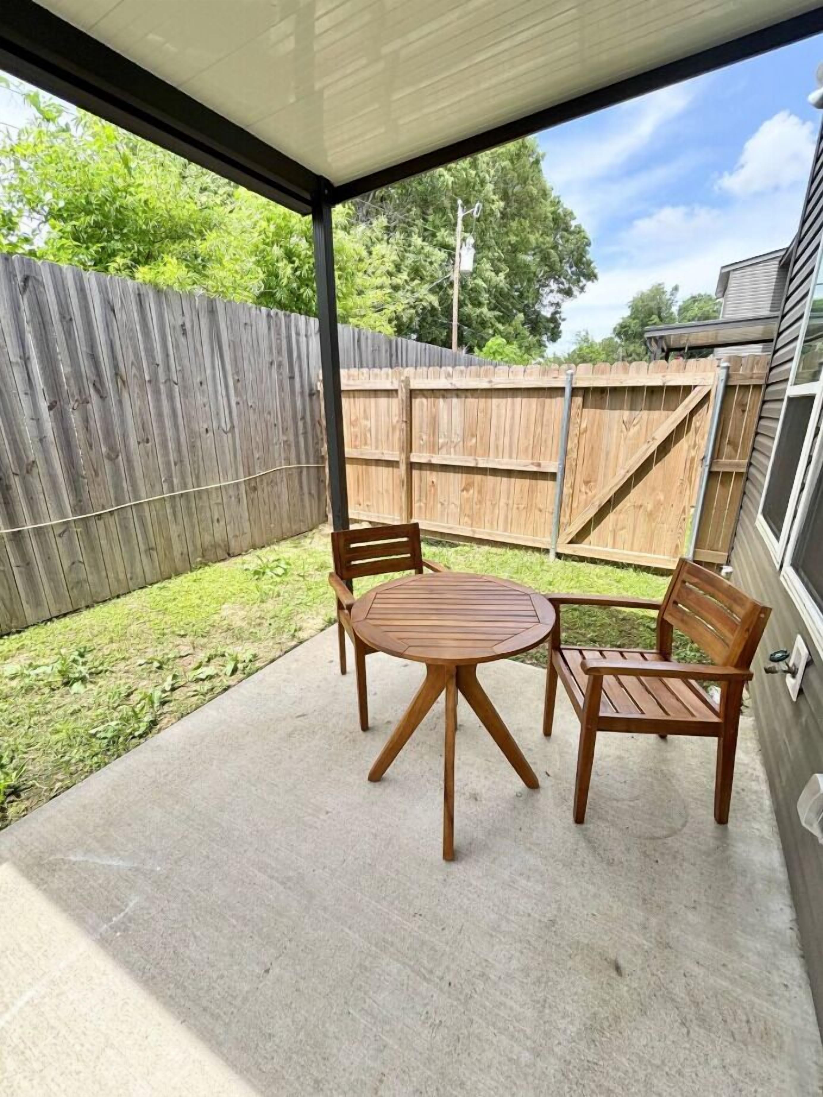 A covered patio area with a round wooden table and two wooden chairs.