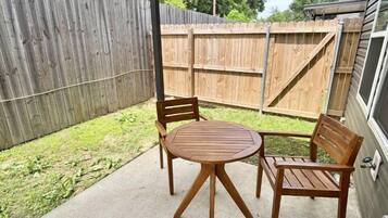 A covered patio area with a round wooden table and two wooden chairs.