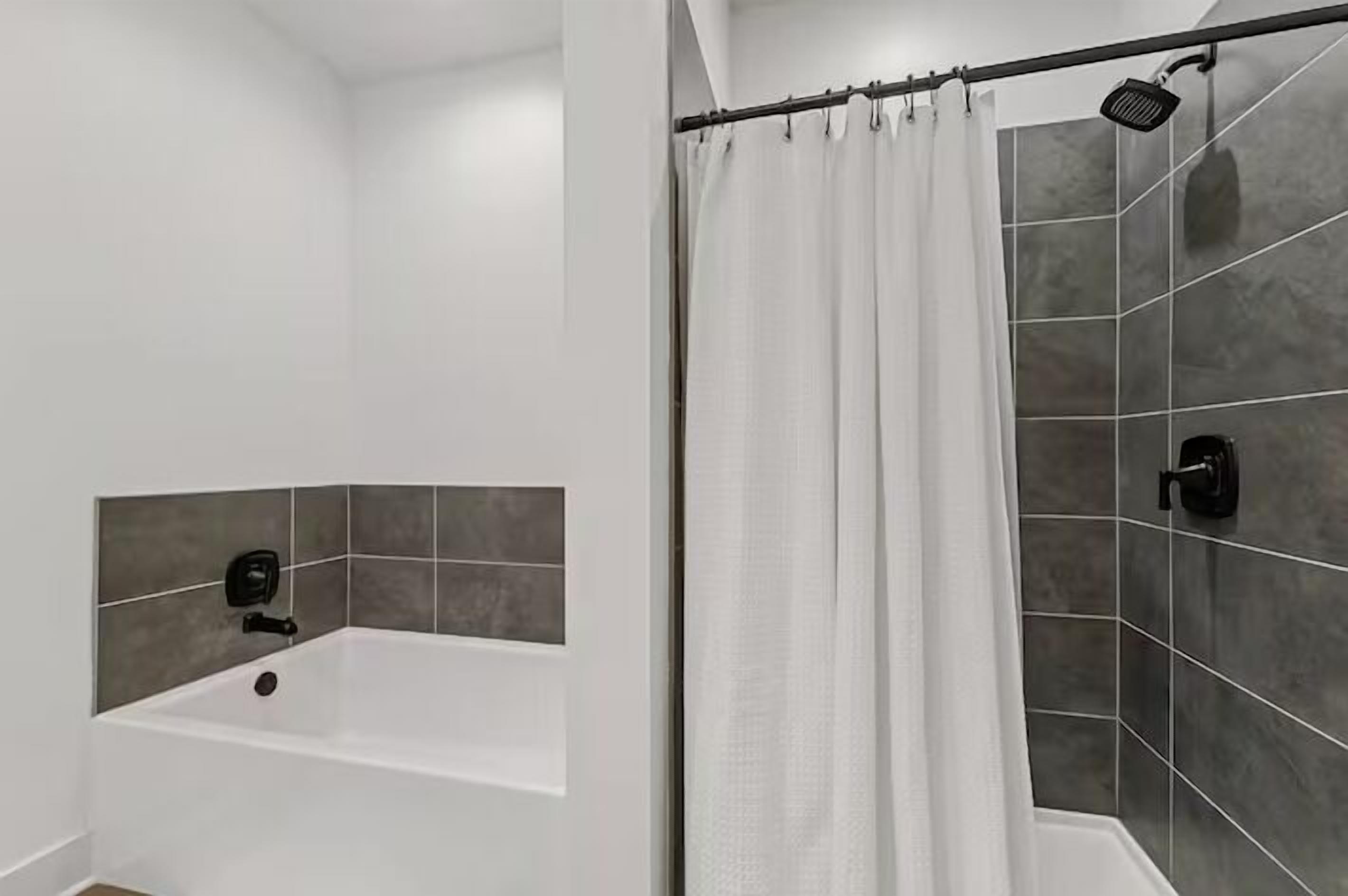 Een moderne badkamer met een badkuip, douche en grijstegel wanden.