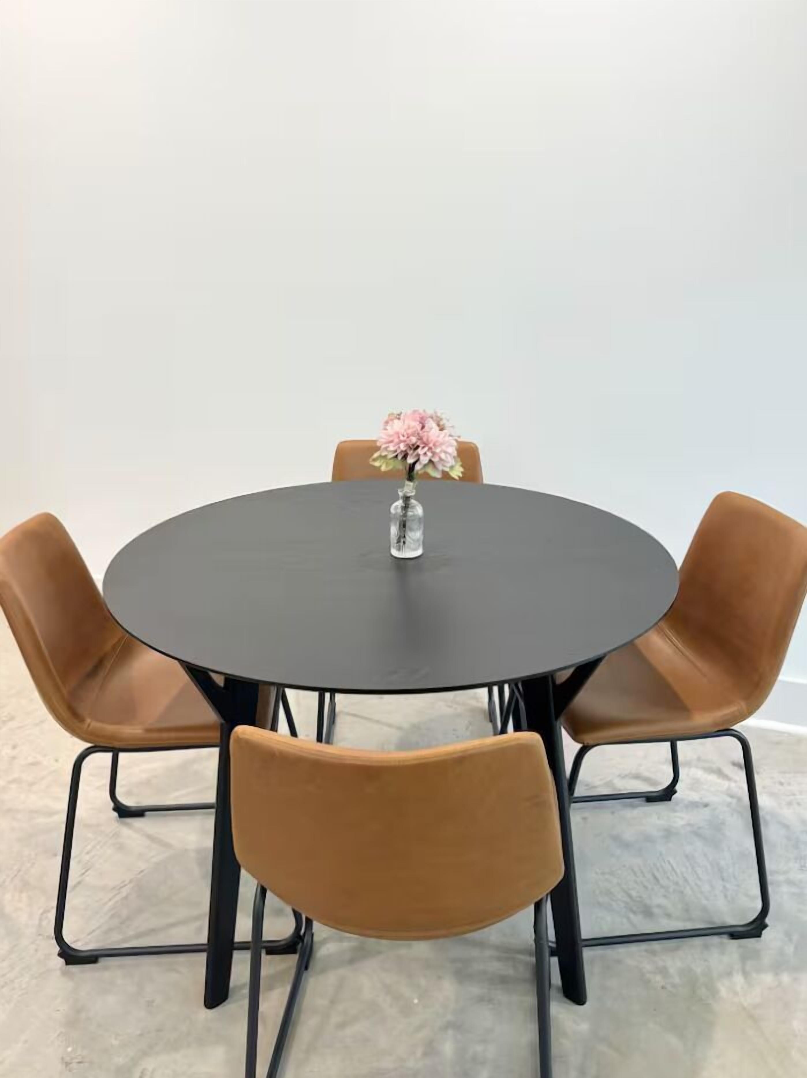 Ein runder Tisch mit Blumen in einer Vase, umgeben von vier braunen Stühlen mit Metallgestellen.