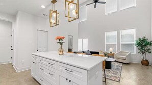 A spacious living area with a large white island, a ceiling fan, and a view of the outside through large windows. - Enclave 2 Bedroom Luxury Homes (Lafayette)