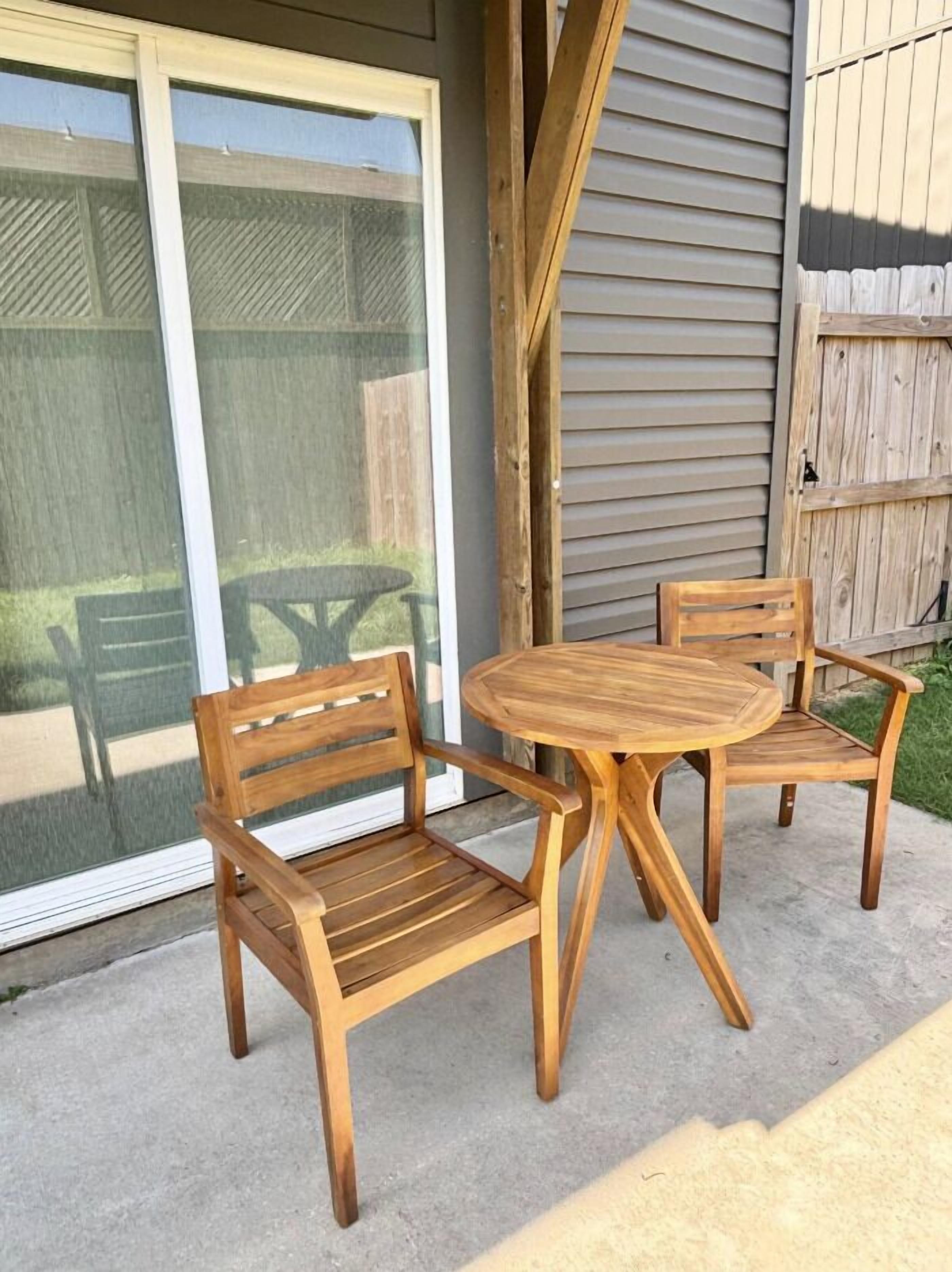 A patio with a wooden table and two chairs, a sliding glass door, and a wooden fence.