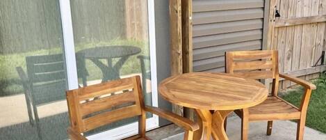 A patio with a wooden table and two chairs, a sliding glass door, and a wooden fence.