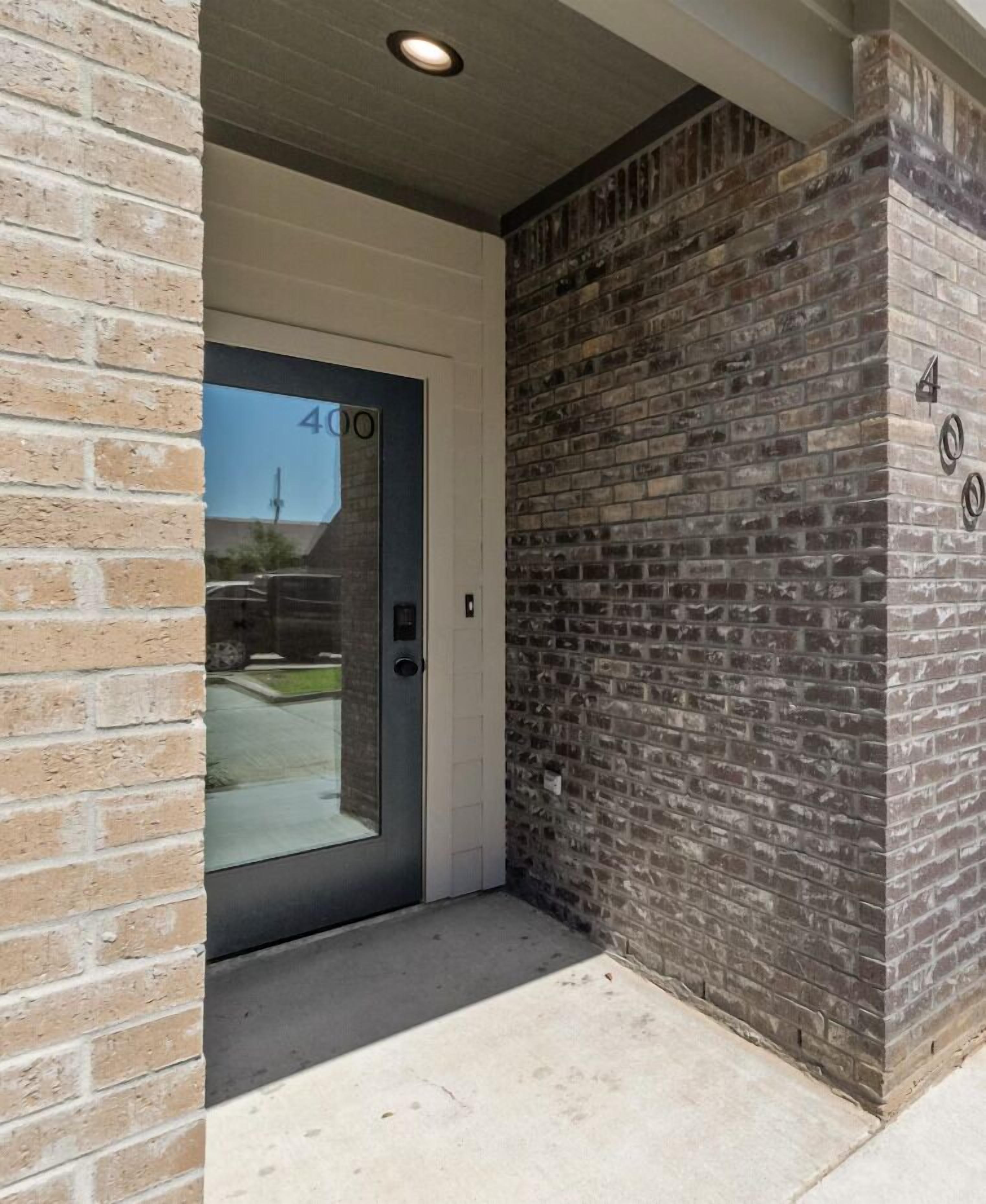 Una entrada de edificio con puerta de cristal, paredes de ladrillo y suelo de hormigón.