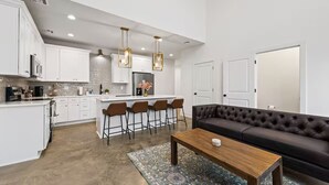 A modern kitchen with white cabinets, a central island with bar stools, and pendant lighting. - Enclave 2 Bedroom Luxury Homes (Lafayette)