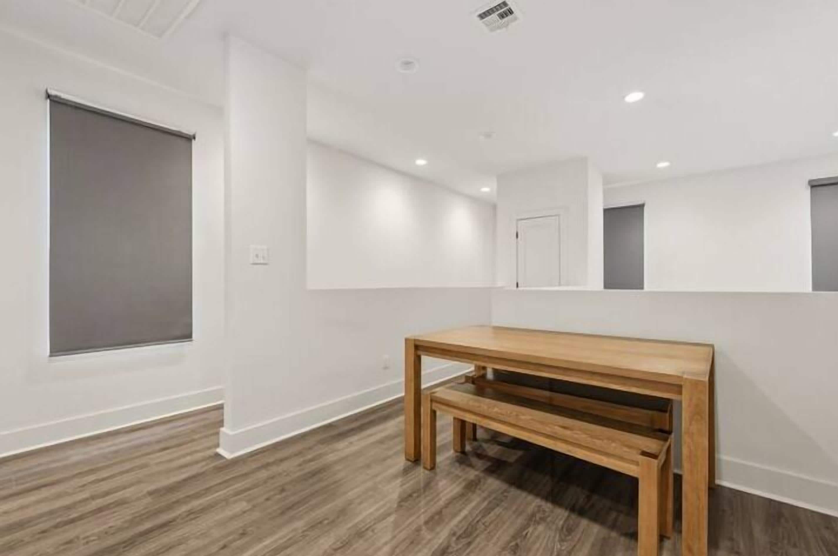 A room with a wooden bench, white walls, and a large window.