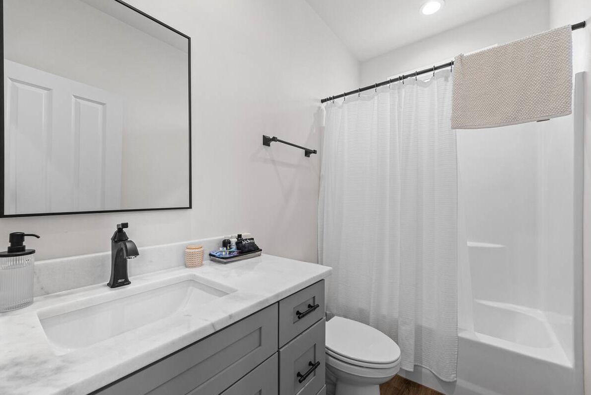 A modern bathroom with a white sink, a black faucet, a toilet, and a shower curtain.