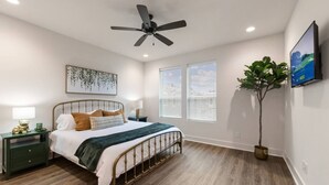 A bedroom with a bed, nightstands, a ceiling fan, a large window, and a potted plant. - Enclave 2 Bedroom Luxury Homes (Lafayette)