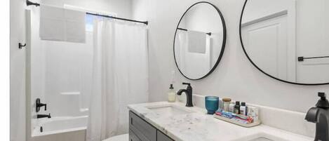 Un baño moderno con bañera, inodoro y tocador con lavamanos y espejos.