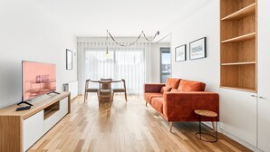 Un salon moderne avec un plancher en bois, un canapé, un téléviseur et une table à manger avec des chaises.