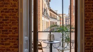 A room with a brick wall, a bed, and a balcony with a table and chairs. - Uma Suites Fuencarral (Madrid)