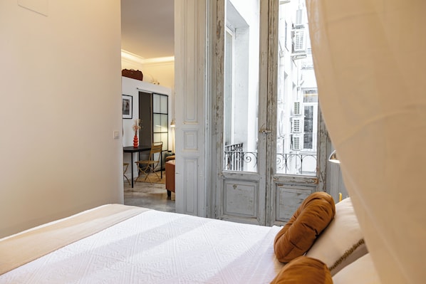 A bedroom with a bed, a view of the street, and a door leading to another room. - Uma Suites Fuencarral (Madrid)