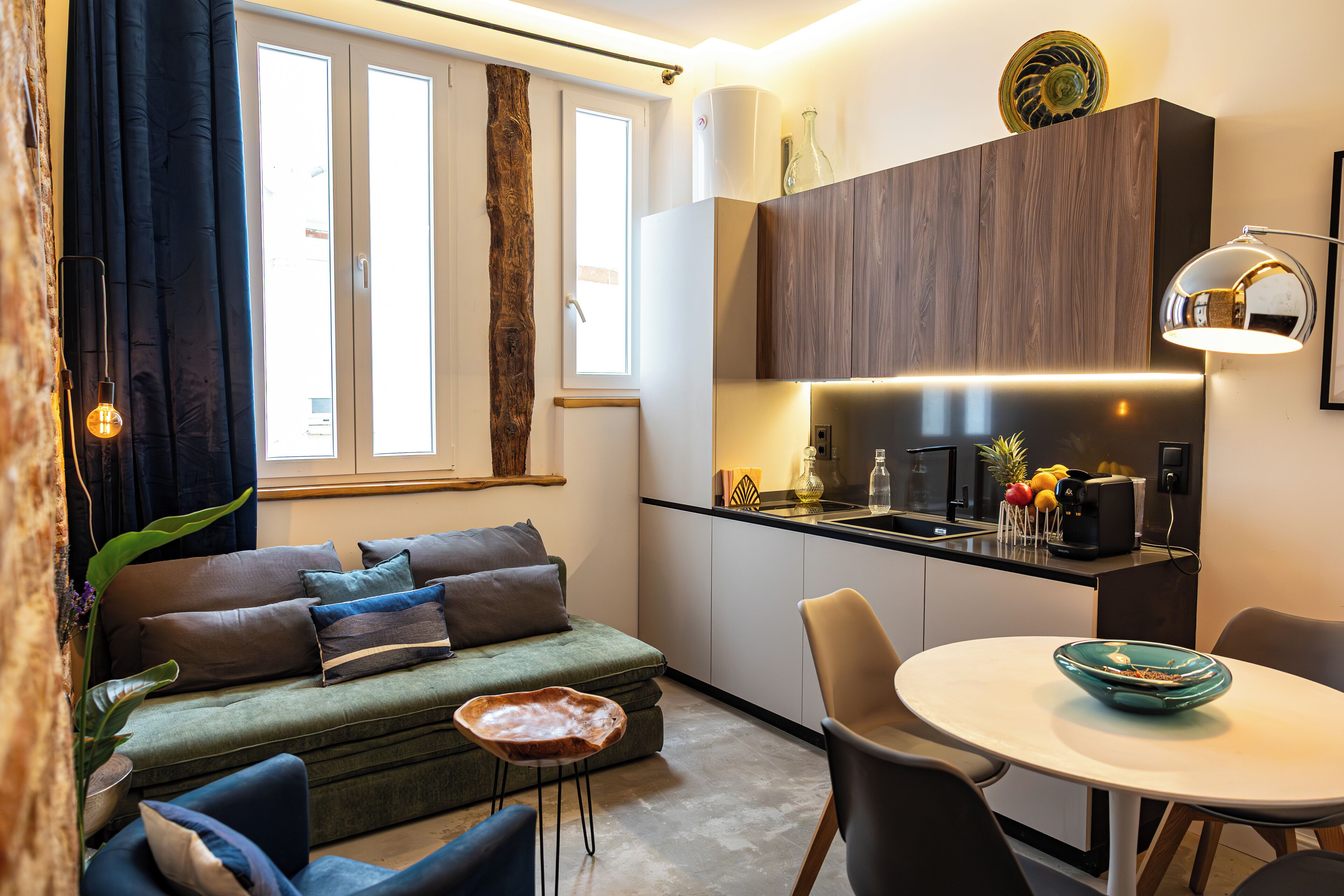 Una sala de estar moderna con un sofá verde, una mesa de comedor con sillas y una zona de cocina con un fregadero y encimera.