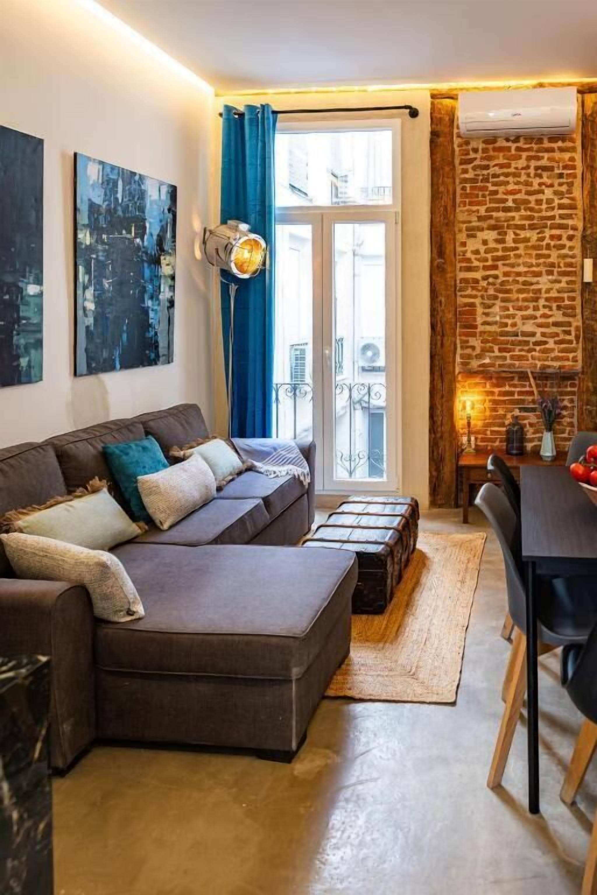 Una sala de estar moderna con un sofá seccional, una mesa de comedor y una pared de acento de piedra.