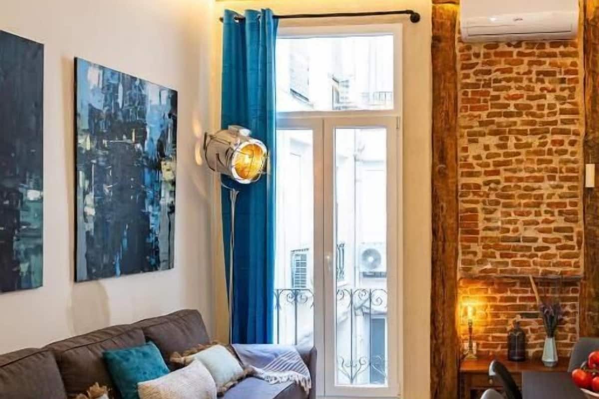 Una sala de estar moderna con un sofá seccional, una mesa de comedor y una pared de acento de piedra.