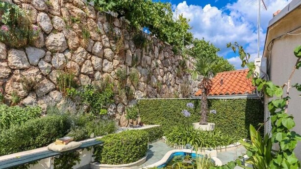 A stone wall with greenery, a pool, and a tiled patio area. - Sunny Palace Studio 2 (Dubrovnik)