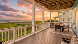 A covered outdoor area with a wooden deck, a table with chairs, and a view of the ocean and beach.