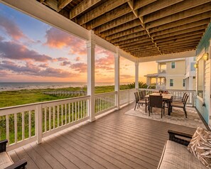A covered outdoor area with a wooden deck, a table with chairs, and a view of the ocean and beach. - Beachfront | First Row Views | Sleeps 16 | Hot Tub (Galveston)