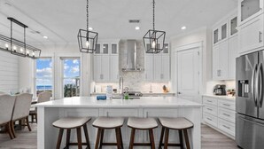 A modern kitchen with a large island, white cabinetry, and stainless steel appliances.