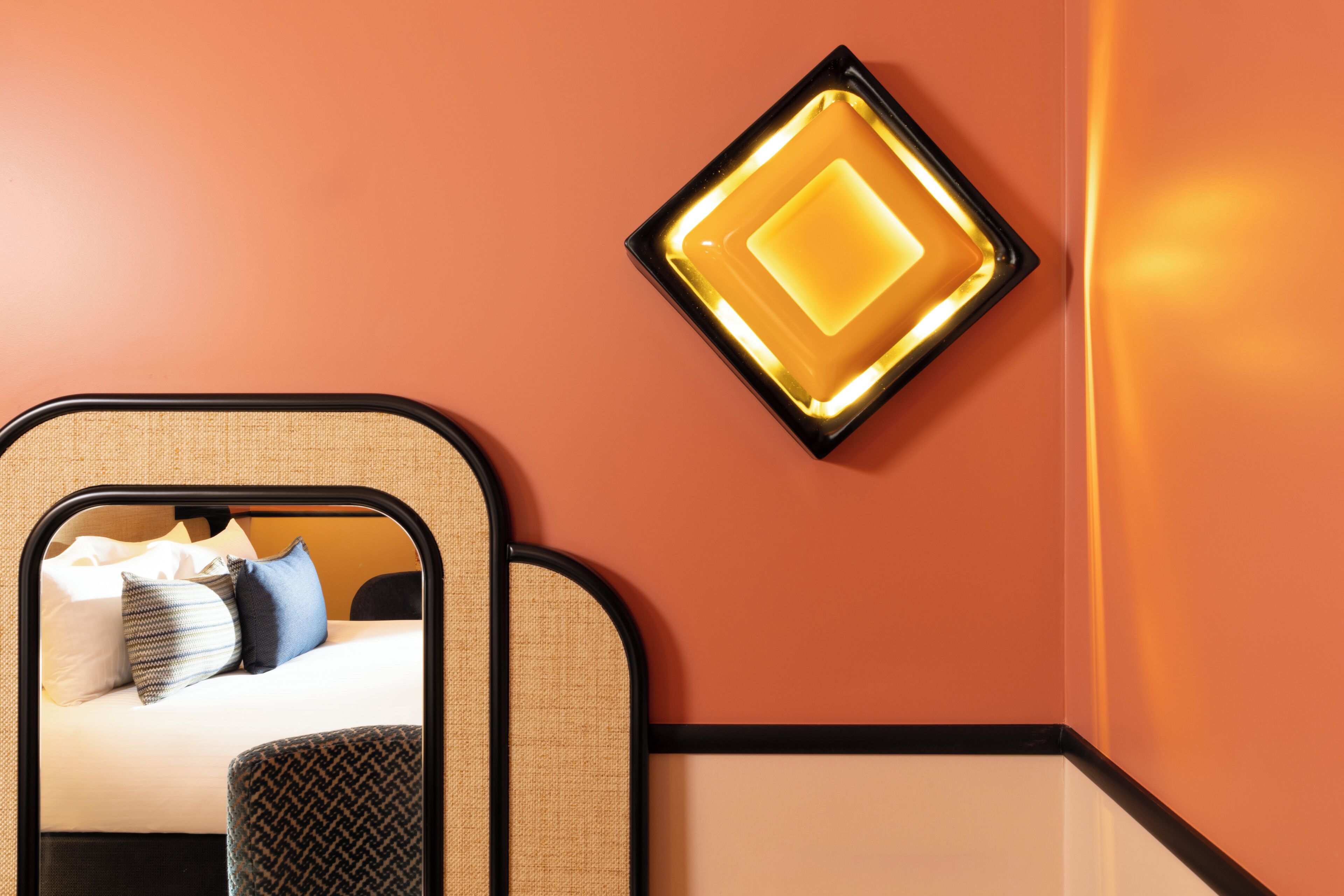Quarto de hotel com uma cama, um espelho e uma luminária fixada na parede.