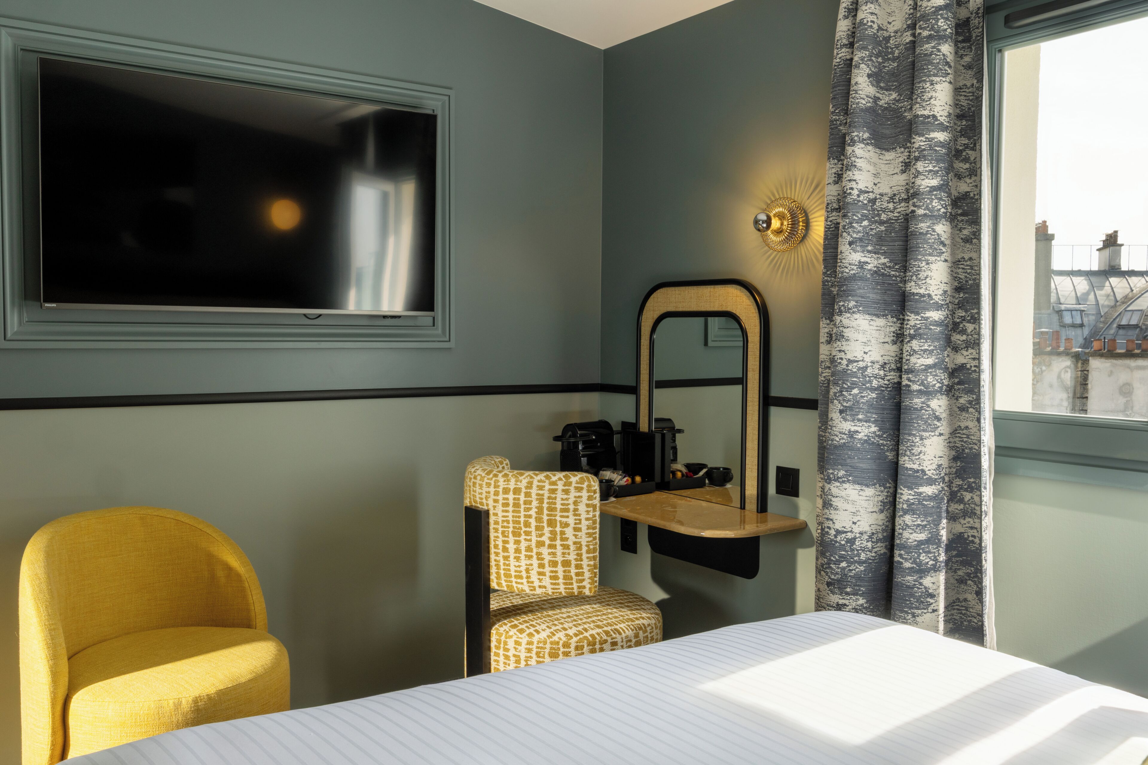 Une chambre d’hôtel avec un lit, une télévision, un miroir, une chaise et une fenêtre avec des rideaux.