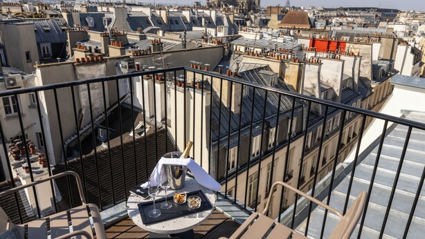 A rooftop terrace with a table set for two, a bottle of champagne, and a view of the cityscape.