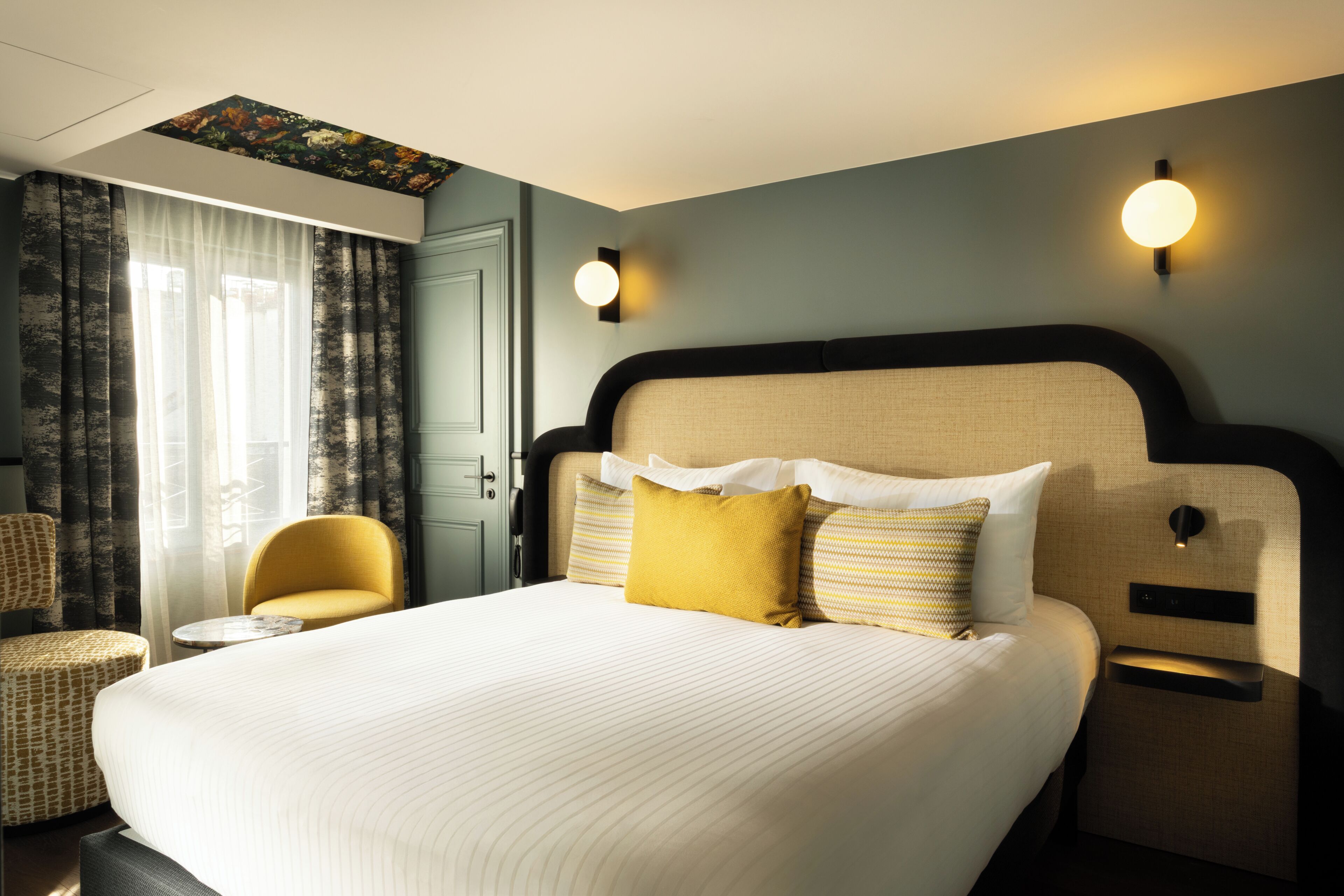 A hotel room with a large bed, a small round table, a chair, and a ceiling light fixture.