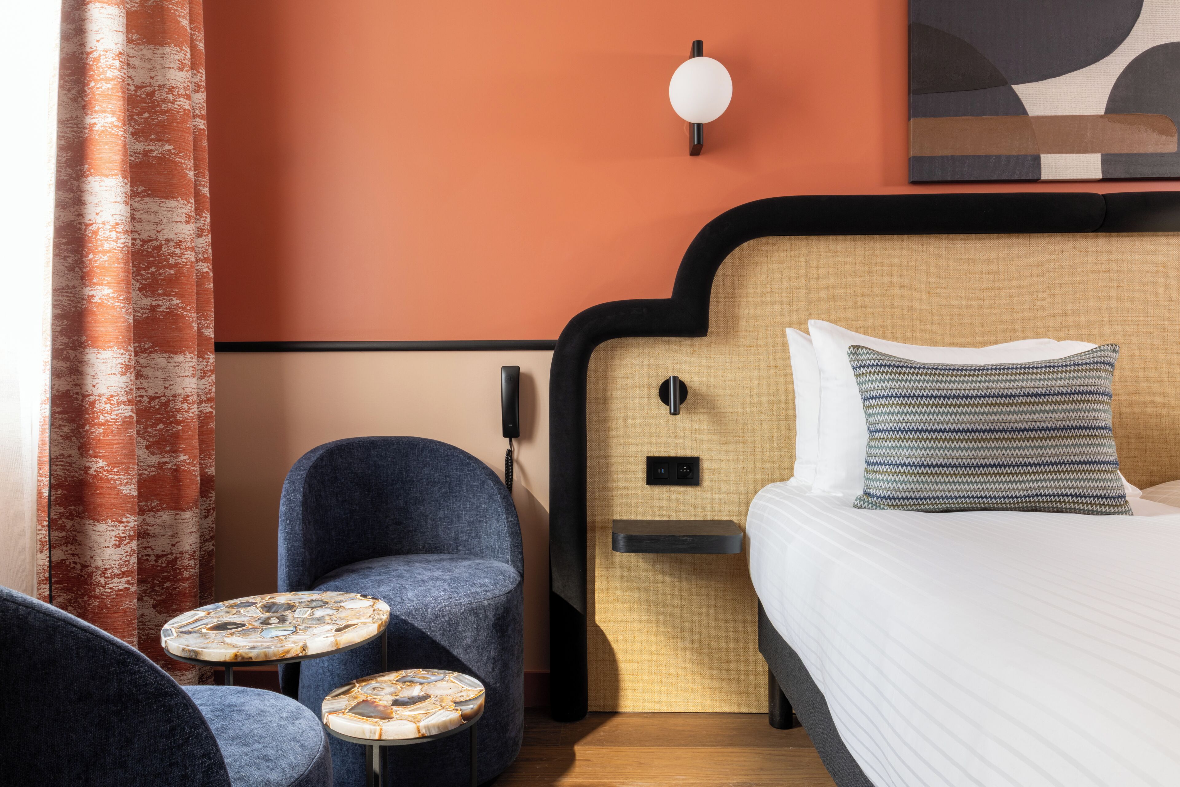 A hotel room with a bed, two armchairs, a small round table, and a wall-mounted light fixture.