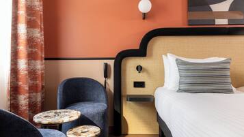 A hotel room with a bed, two armchairs, a small round table, and a wall-mounted light fixture.