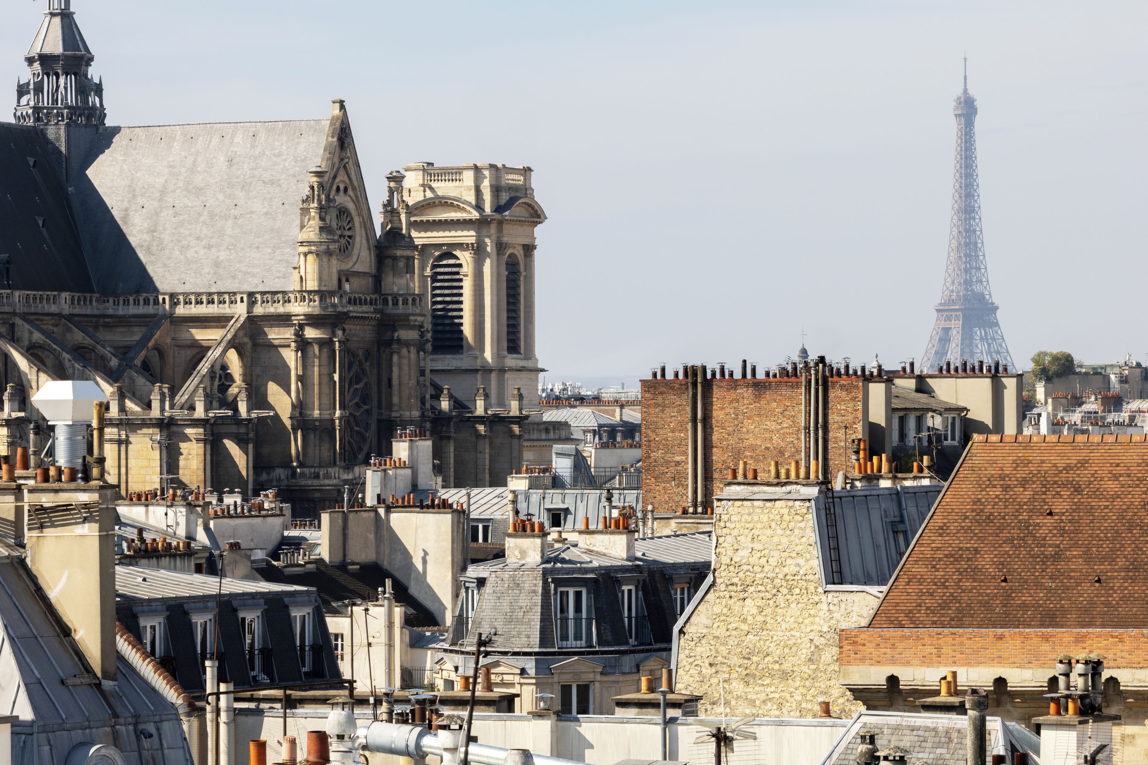 Un bâtiment historique à l’architecture complexe, doté d’une tour imposante, avec la Tour Eiffel en arrière-plan.