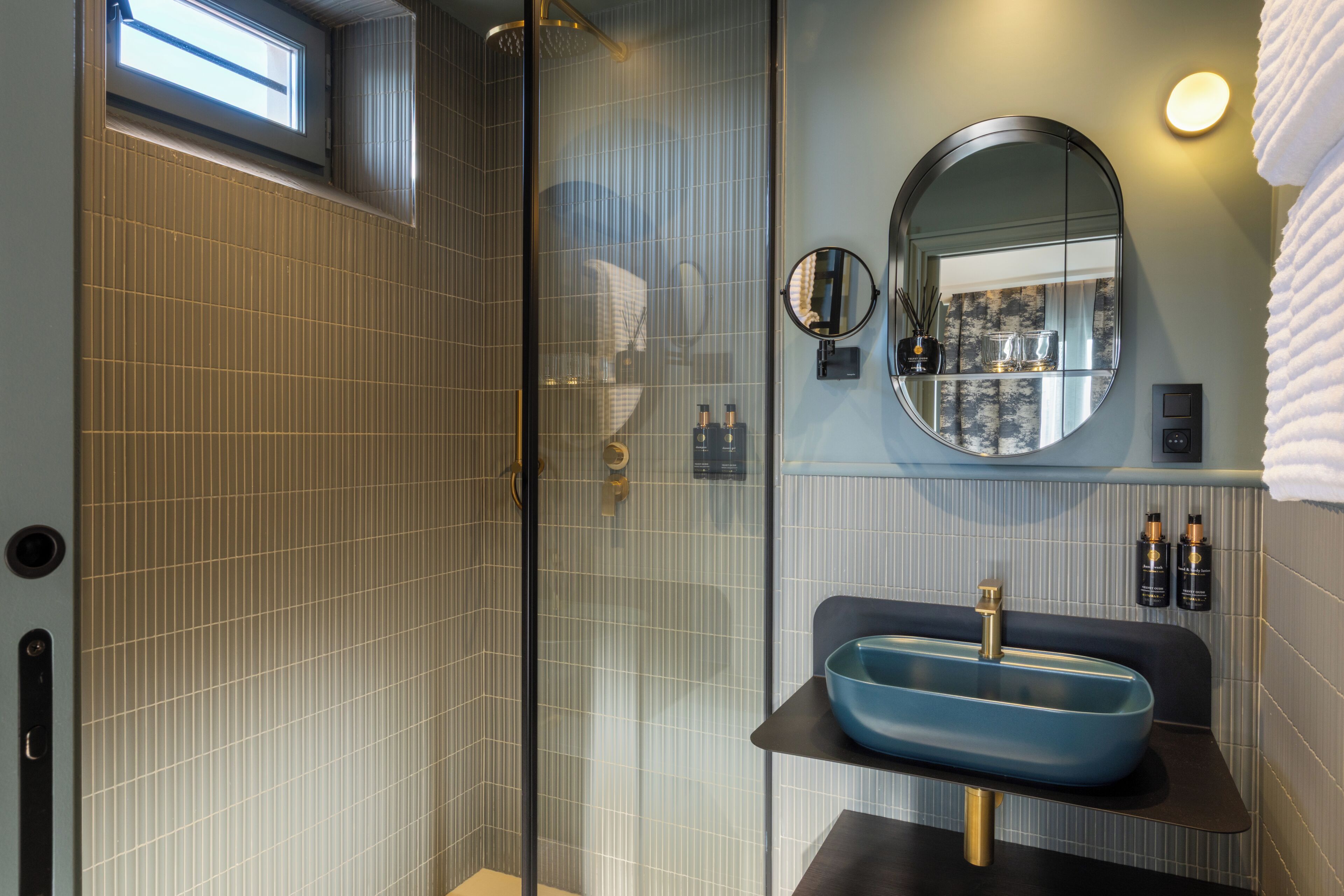 Une salle de bain moderne avec une douche à parois de verre, un lavabo bleu et un miroir rond.