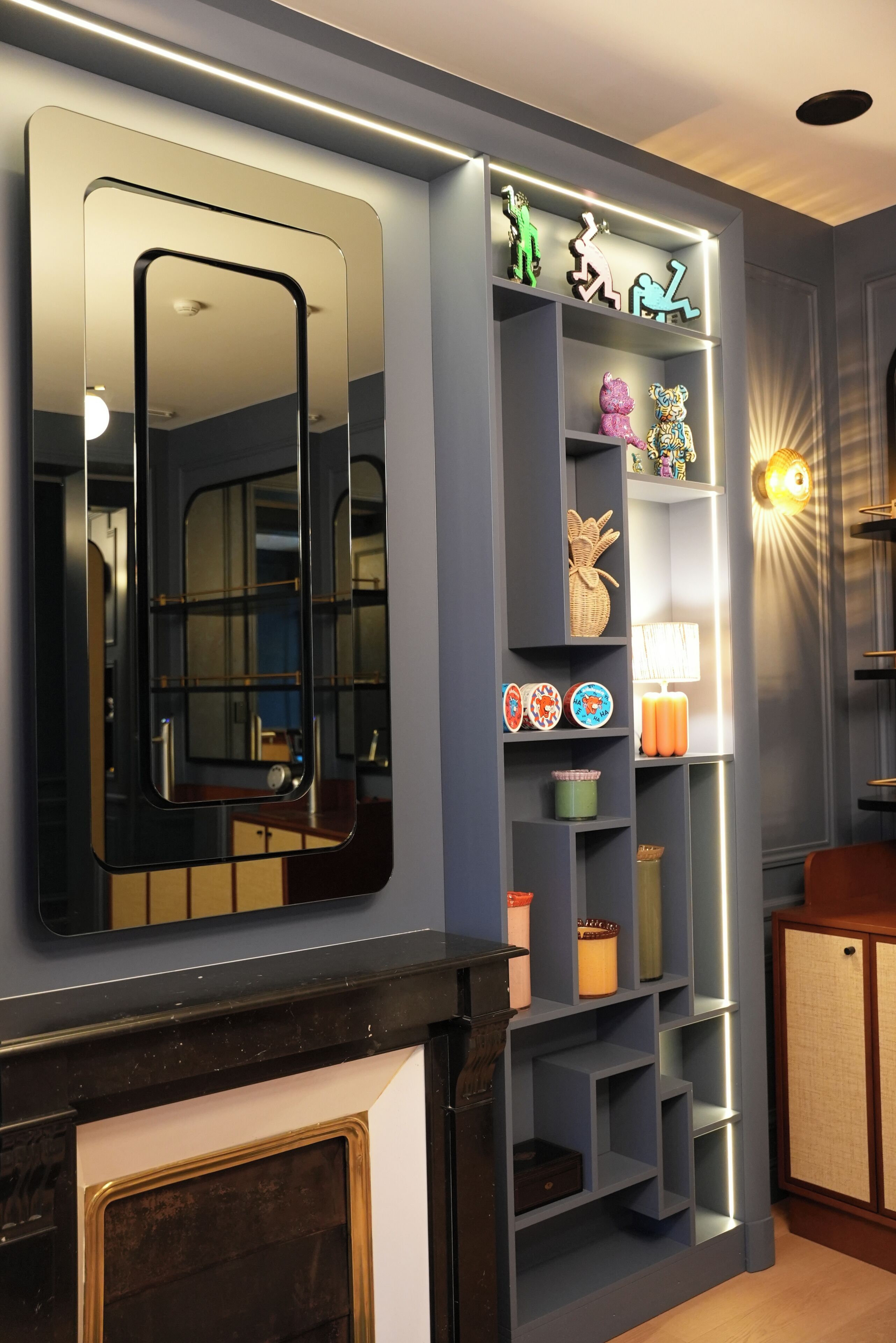 Un intérieur moderne agrémenté d’un grand miroir, d’étagères ornées d’objets décoratifs et d’un luminaire fixé au mur.